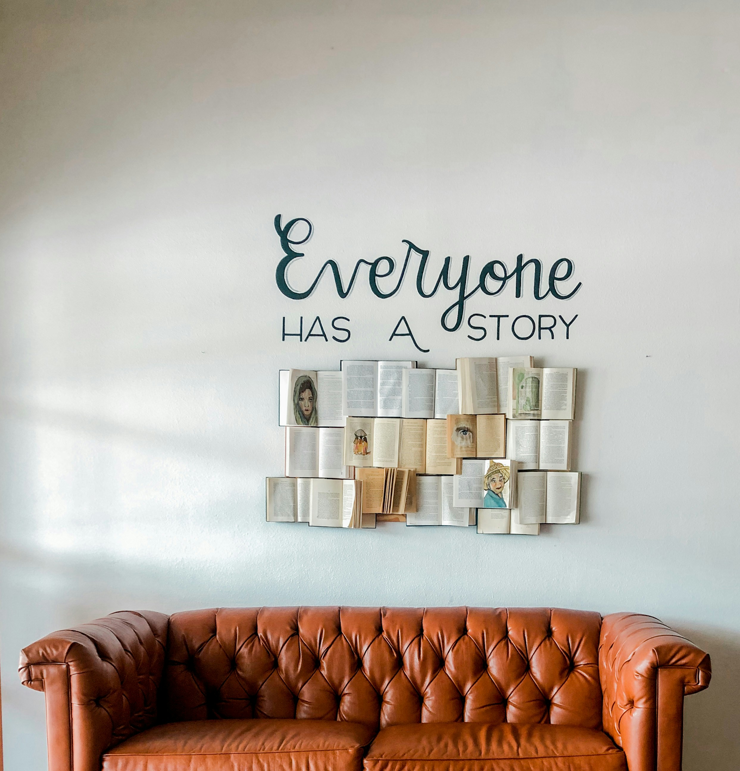 Books arranged on a wall with 'Everyone Has A Story' text above a warm leather couch